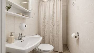 Baño con lavamanos blanco, inodoro y cortina de ducha con estampado de hojas.