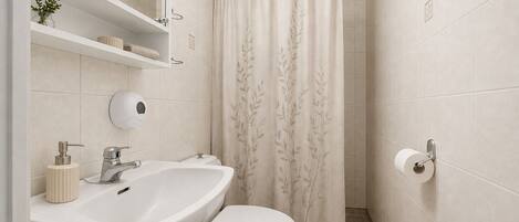 A bathroom with a white sink, toilet, and a shower curtain with a leaf pattern.