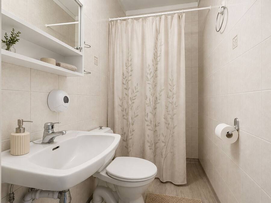 Baño con lavamanos blanco, inodoro y cortina de ducha con estampado de hojas.