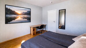 Un dormitorio con cama, escritorio, silla, un cuadro grande enmarco y un espejo.