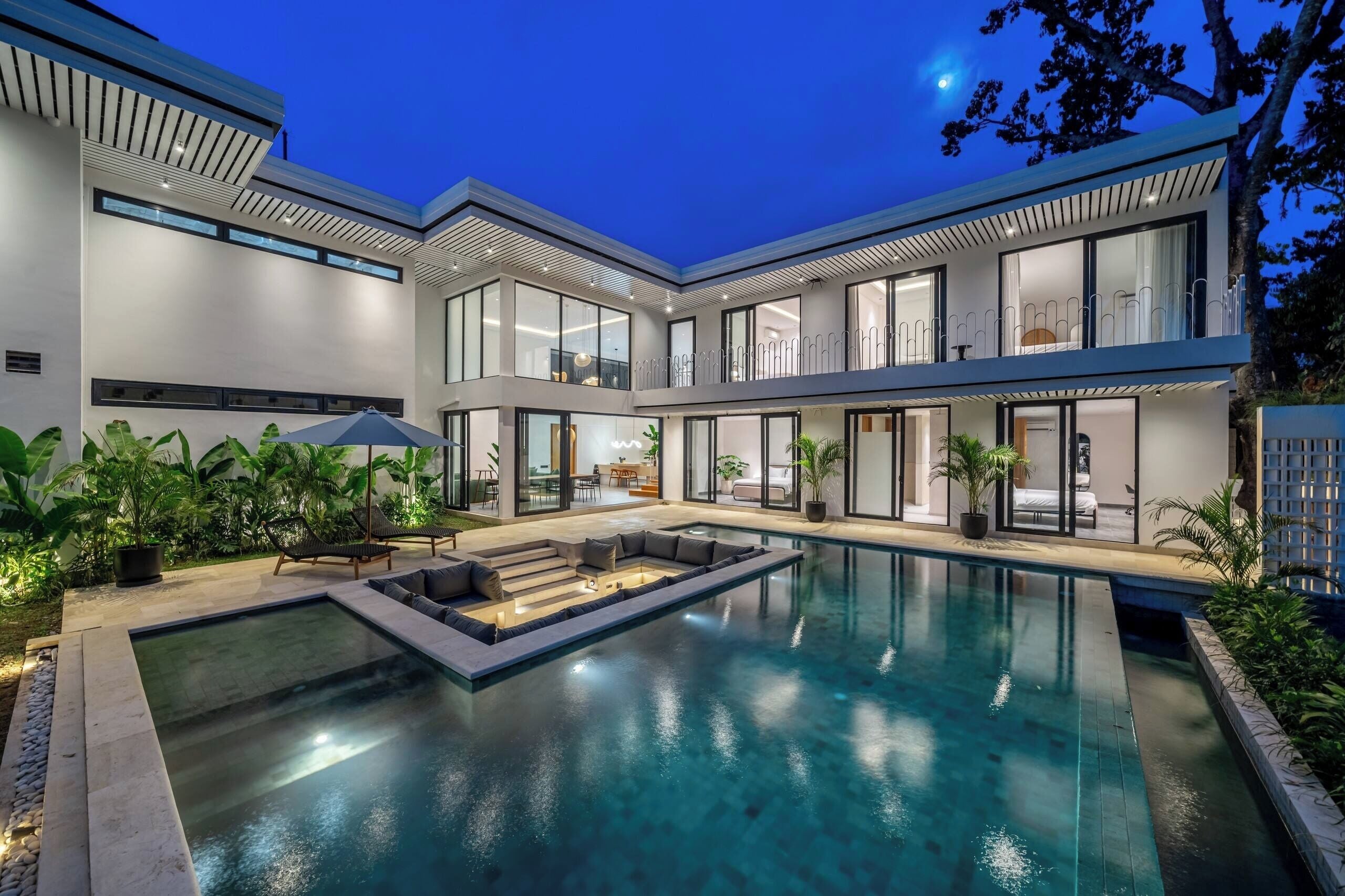Ein modernes Haus mit Swimmingpool, Sitzgelegenheit im Freien und großen Fenstern.