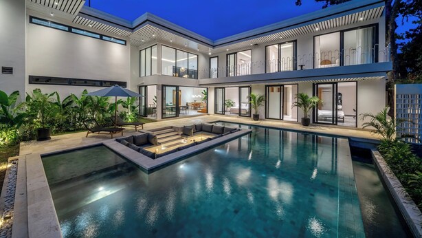 Une maison moderne dotée d’une piscine, d’un espace salon extérieur et de grandes fenêtres.