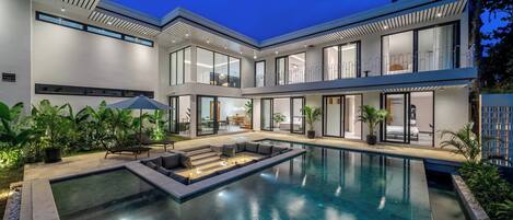 A modern house with a swimming pool, outdoor seating, and large windows.