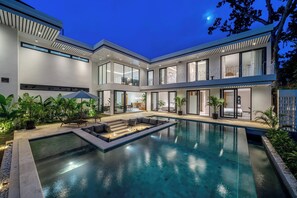 Una casa moderna con piscina, area salotto esterna e ampie vetrate.