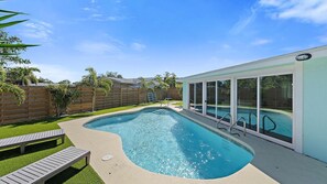 A swimming pool with a curved edge, a wooden deck, and a glass-enclosed building.