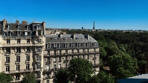 A multi-story building with balconies, a clear view of the Eiffel Tower in the background, and surrounding greenery. - Charming studio apartment in Neuilly – Jardin d'Acclimatation (Neuilly-sur-Seine)