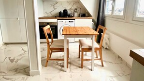 A modern kitchen with a wooden table and chairs, a built-in oven, and a window with curtains. - Charming studio apartment in Neuilly – Jardin d'Acclimatation (Neuilly-sur-Seine)