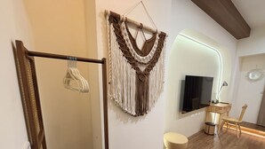 Una habitación moderna con suelo de madera, un tapiz de macramé, un televisor de pantalla plana, una silla de madera y un taburete redondo.