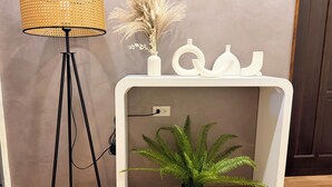 Une pièce comprenant une console blanche, une fougère en pot, un grand lampadaire et divers objets décoratifs.