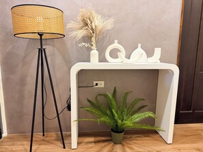 A room with a white console table, a potted fern, a tall floor lamp, and decorative items.