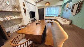 Un salon moderne avec une table à manger en bois, un canapé et un téléviseur fixé au mur.