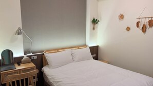 Une chambre d’hôtel bien rangée, avec un lit, une table de chevet, une lampe et une petite chaise en bois.