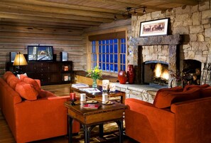 A log cabin interior with a stone fireplace, a television, and a cozy seating area.