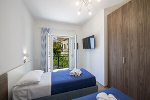 Ein Schlafzimmer mit Bett, Fernseher, Kleiderschrank und einem Balkon mit Blick auf Gebäude.