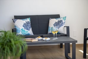 Ein moderner Außenbereich mit einer Couch, Kissen, einem Tisch und einem Glas Wein.