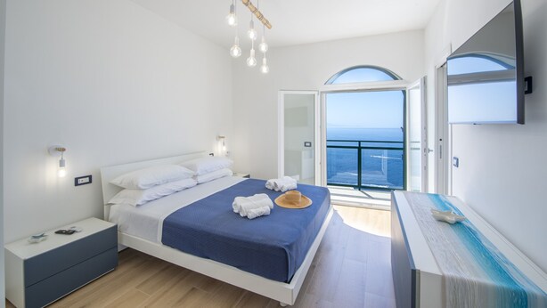 A modern bedroom with a bed, bedside table, and a view of the sea. - Villa Cristal - Sea View Villa With Private Garden (Praiano)