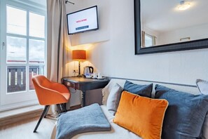 A hotel room with a sofa, a chair, a TV, a lamp, and a window. - Lakeside Hotel SEEHOF I Lounge & Living (Zell am See)