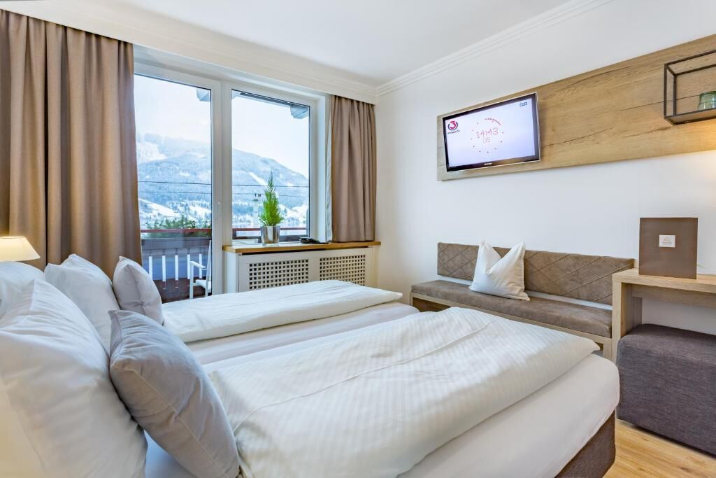 Quarto de hotel com duas camas, televisão, janela com vista para montanhas e varanda com planta.