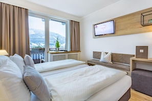 A hotel room with two beds, a TV, a window with a view of mountains, and a balcony with a plant. - Lakeside Hotel SEEHOF I Lounge & Living (Zell am See)