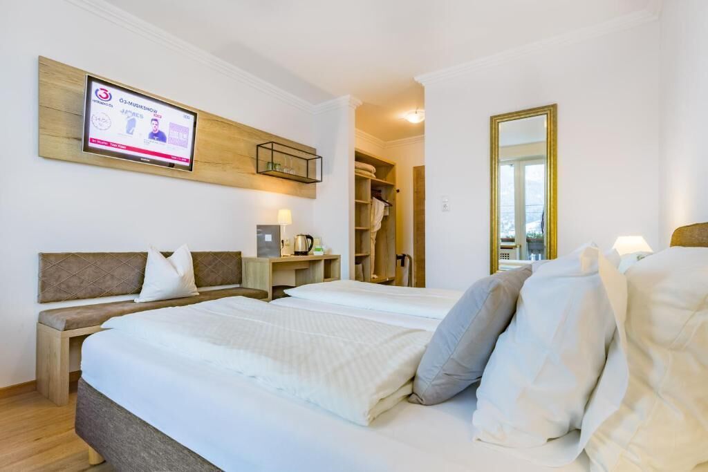 A hotel room with a bed, a desk, a TV mounted on the wall, a mirror, and a wardrobe.