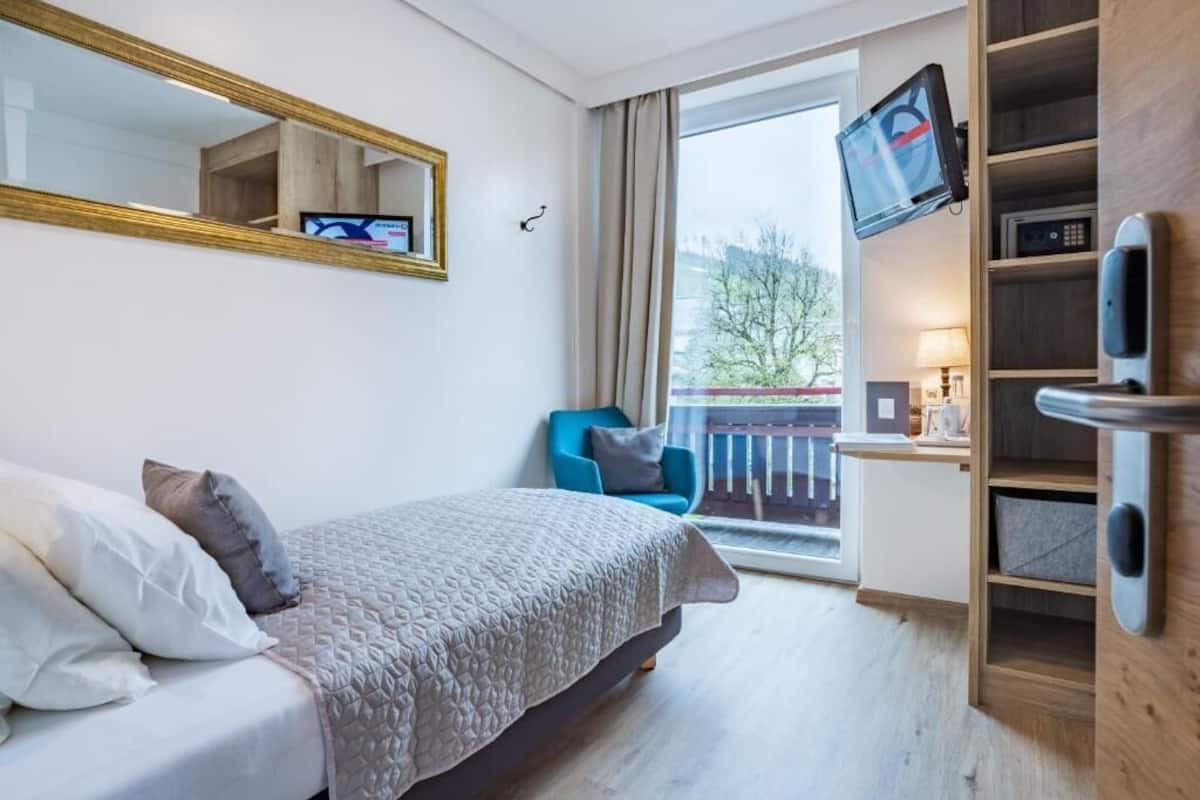 Ein Hotelzimmer mit Bett, Fernseher, Schreibtisch mit Computer, Stuhl und einem Balkon mit Geländer.
