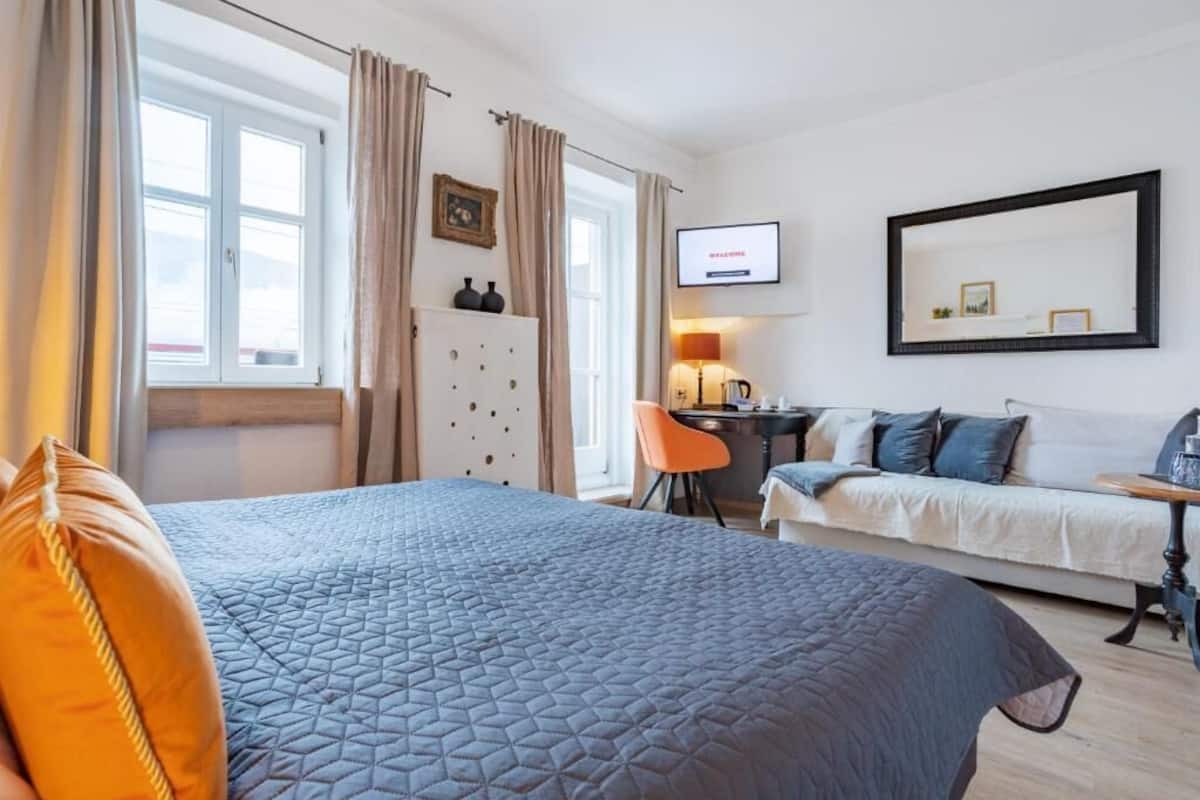 Ein Hotelzimmer mit Bett, Schreibtisch, Sessel, Sofa und einem an der Wand befestigten Fernseher.