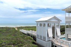 A white beach house with a deck leading to a small tower, overlooking the ocean.