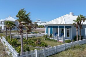 A coastal house with a white fence, palm trees, and a patio with outdoor furniture.