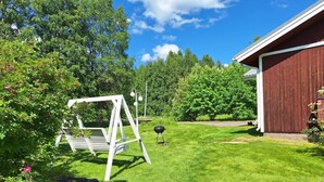 A well-maintained lawn with a swing set, a barbecue grill, and a wooden building. - Sun's Tupa - Traveller's Marmalade (Siikalatva)