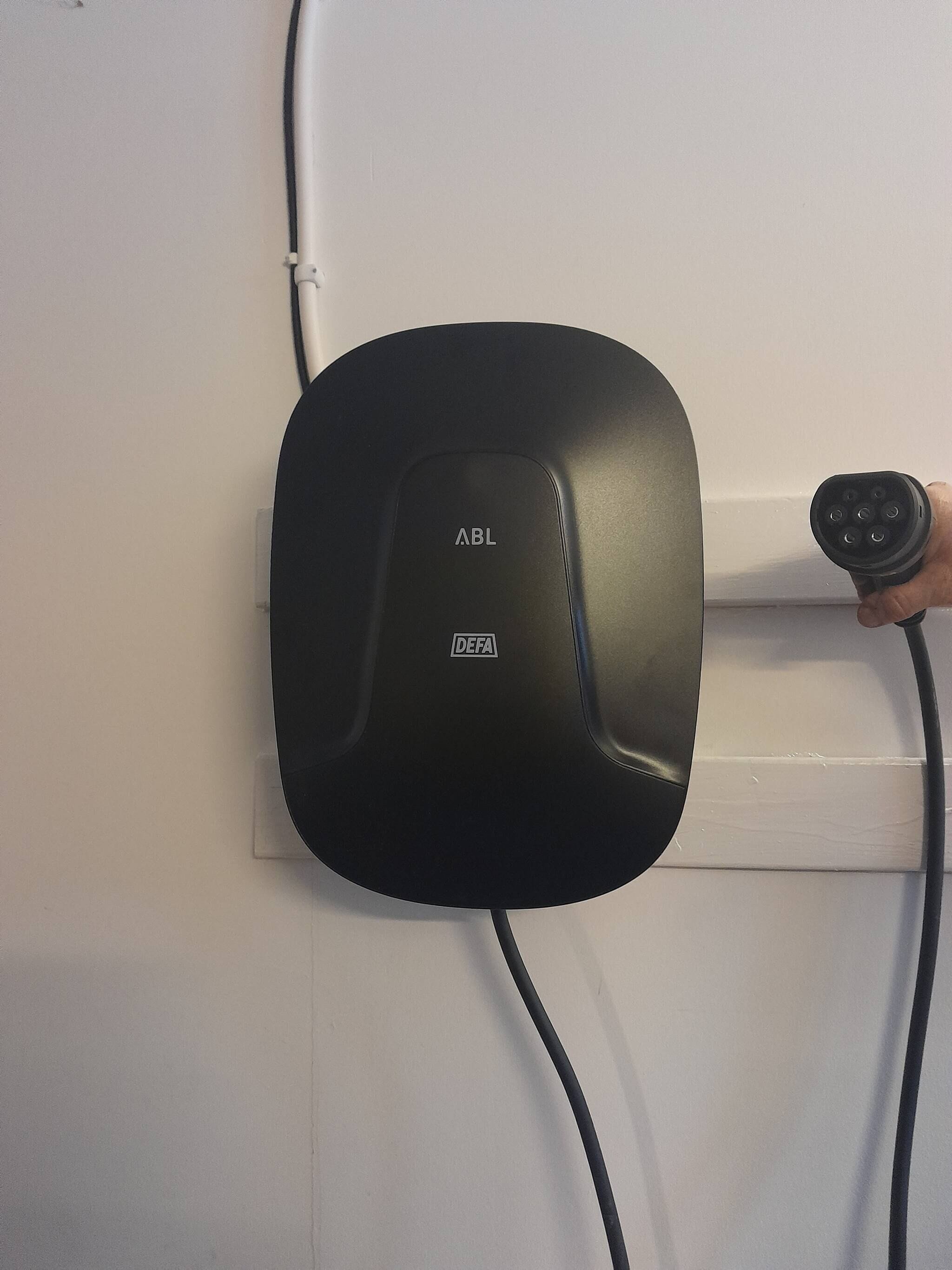 A black charging station with 'ABL' and 'DEFA' labels, connected to a wall socket.