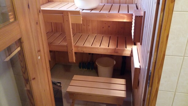 A wooden sauna with benches, a small table, and a bucket. - Sun's Tupa - Traveller's Marmalade (Siikalatva)