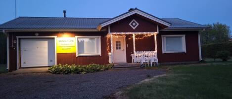 A building with a garage, a porch with chairs, and a sign for Sunin Tupa travel accommodation.