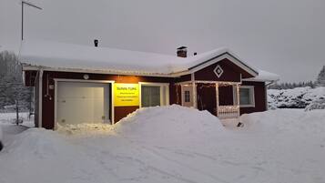 A small, single-story building with a garage door, a porch with lights, and a sign indicating it is a travel accommodation.