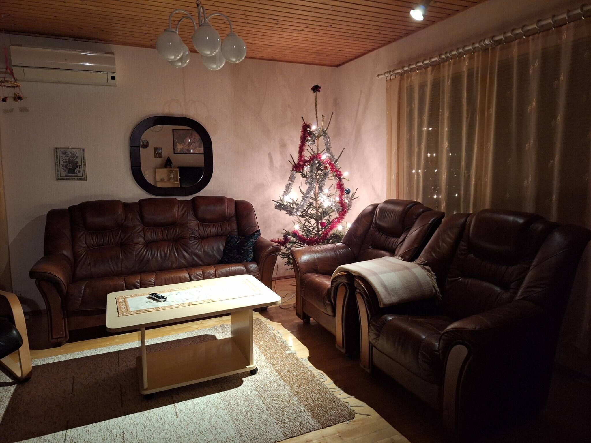 A living room with a brown leather sofa, a matching armchair, a coffee table, a Christmas tree, and a mirror on the wall.