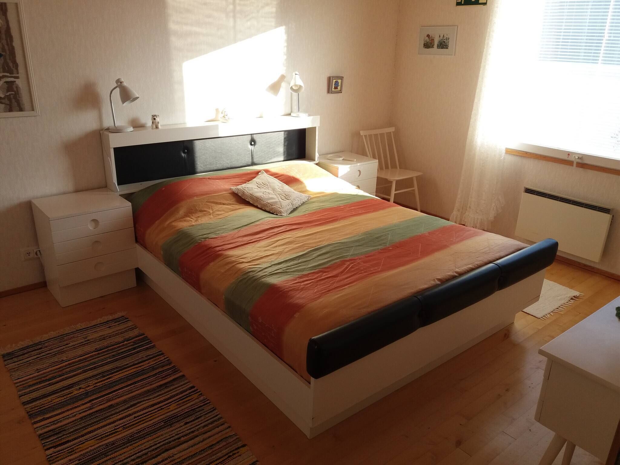 A bedroom with a bed, bedside tables, a chair, a desk, and a window.