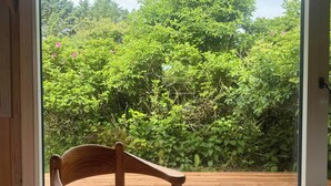 A wooden chair facing a sliding glass door leading to a wooden deck with a lush green garden view. - House in Kettrup Bjerge near nature and the sea (Kettrup Bjerge)