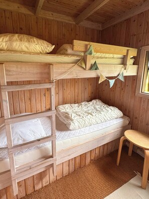 Une chambre avec un lit superposé, un plafond et des murs en bois, un petit tabouret et une fenêtre.