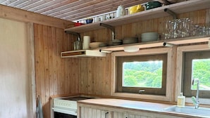 A wooden cabin-style kitchen with a window, a sink, and a dining area with a table and chairs. - House in Kettrup Bjerge near nature and the sea (Kettrup Bjerge)