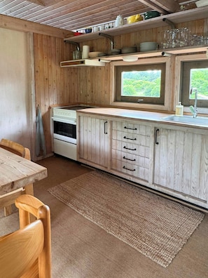 A wooden cabin-style kitchen with a window, a sink, and a dining area with a table and chairs.