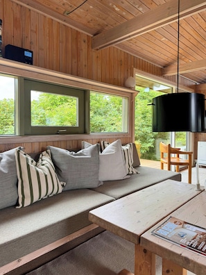 Un intérieur en bois avec un canapé, des coussins, une table et un luminaire suspendu.