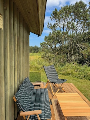 A wooden deck with two striped lounge chairs and a small table, overlooking a grassy area with trees.