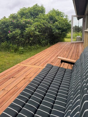 A wooden deck with a sofa and a table, surrounded by greenery.