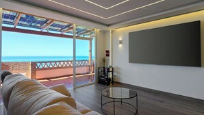 Una sala de estar moderna con un ventanal grande con vista al mar, un sofá, una mesa de centro y un televisor de pantalla plana.
