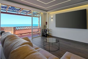 Ein modernes Wohnzimmer mit großem Fenster zum Meer, einer Couch, einem Couchtisch und einem Flachbildfernseher.