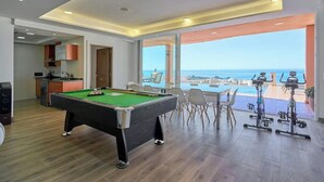 Mesa de billar en una habitación con vistas al mar, zona de comedor y equipo de ejercicio.