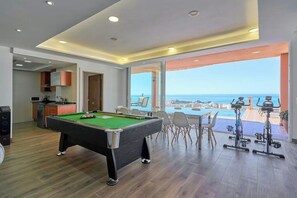 Ein Billardtisch in einem Raum mit Meerblick, einem Essbereich und Fitnessgeräten.