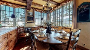 A dining area with a wooden table set for a meal, surrounded by chairs, and large windows offering a view of the outdoors. - Impressive Castle with Great Mountain Views and Foosball in Mammoth Lakes, California (Mammoth Lakes)