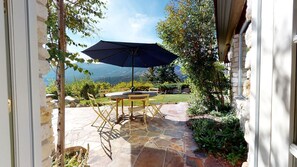 Una terrazza esterna con pavimento in pietra, un tavolo, sedie e un grande ombrellone.