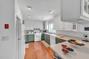 Une cuisine moderne avec des meubles blancs, une cuisinière et un lave-vaisselle. Une fenêtre laisse entrer la lumière naturelle et un petit tapis recouvre le sol.