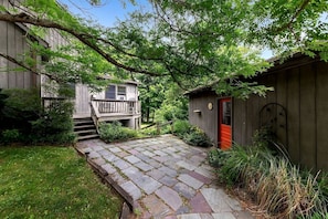A wooden deck with stone tiles, a red door, and a small shed in a garden setting.